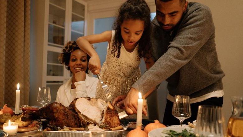 Father, child, mother carve a turkey at Thanksgiving